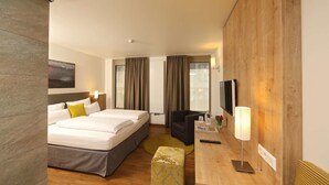 Una habitación de hotel con cama, escritorio, silla, televisor y ventana con cortinas.