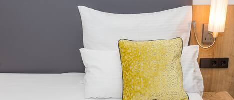 A bed with white and yellow pillows, a grey headboard, and a bedside lamp.