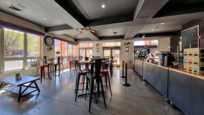 Un interior de cafetería moderna con taburetes, mesas y una barra con una máquina de café.