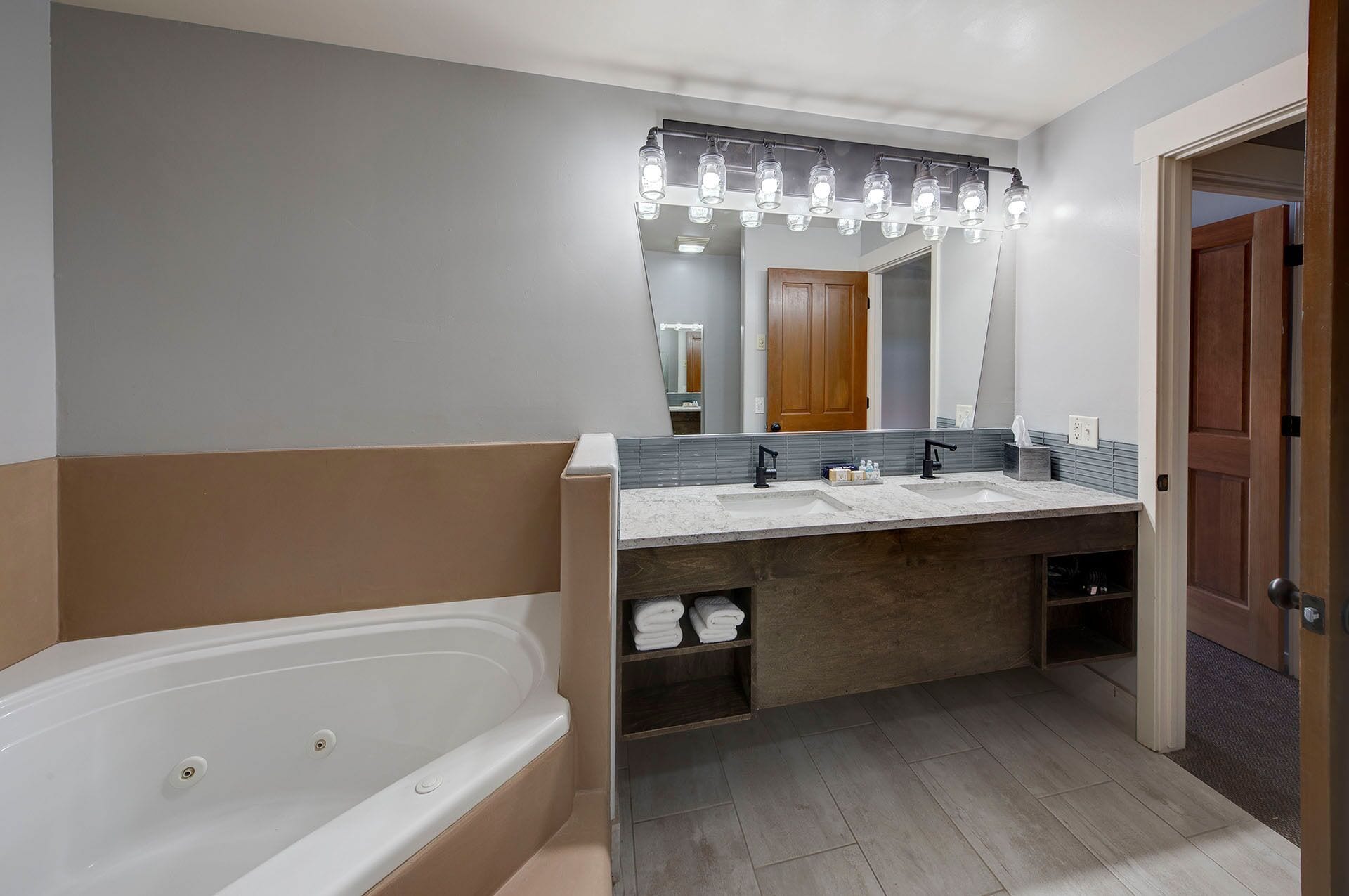 A modern bathroom with a bathtub, double vanity with a mirror, and a wooden shelf with towels.