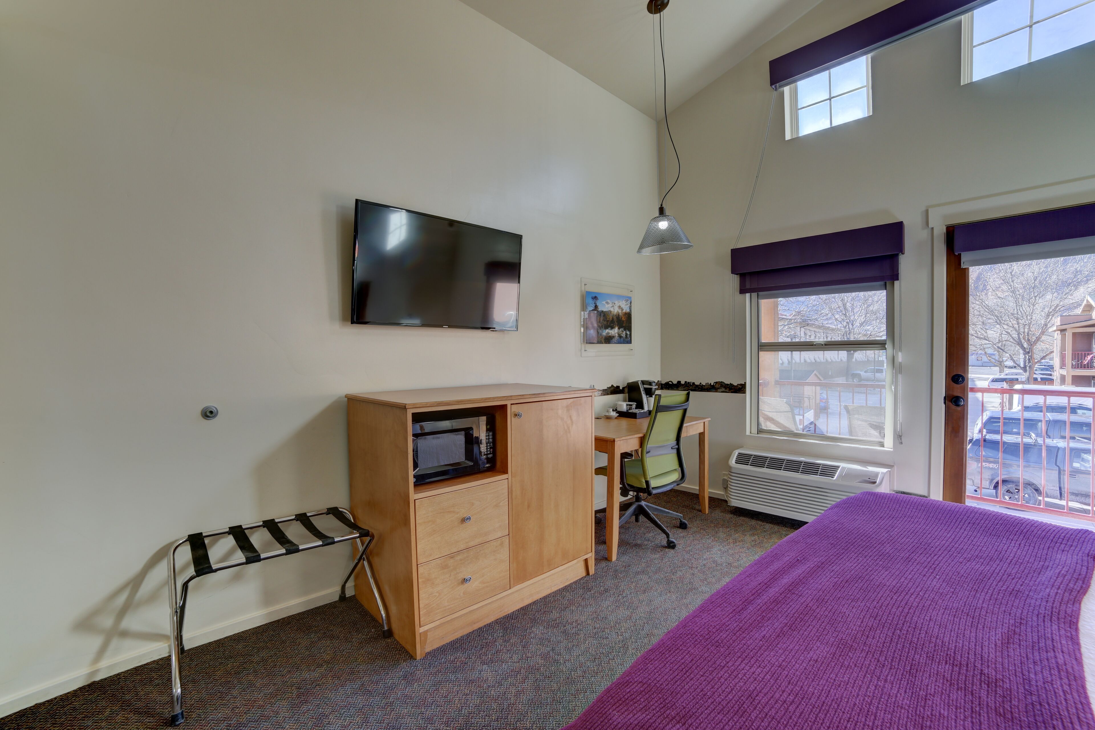 Une chambre à coucher comprenant un lit, un bureau avec une chaise, un téléviseur, une fenêtre avec des stores et un radiateur.