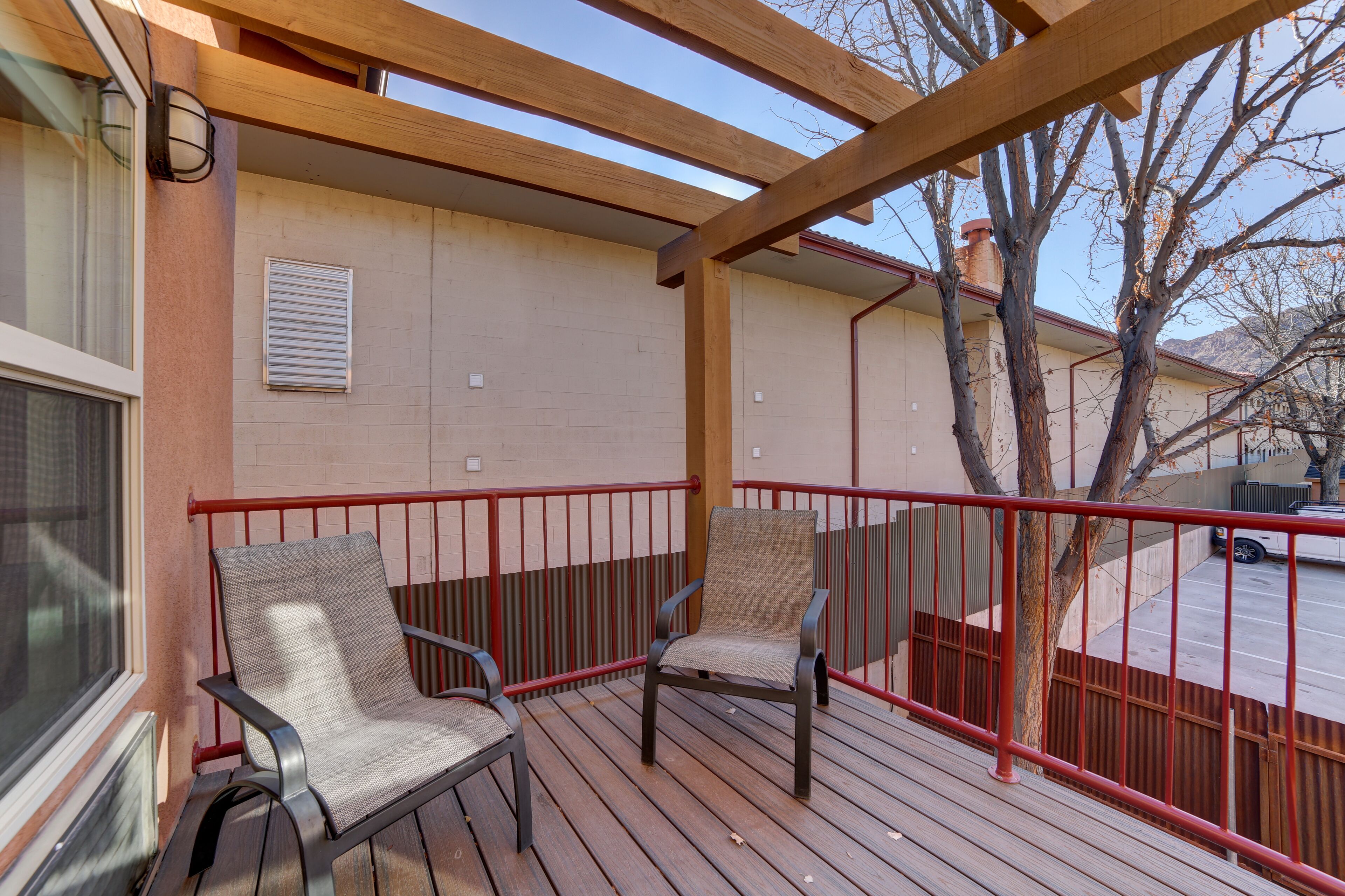 A covered outdoor deck with two chairs and a red railing.