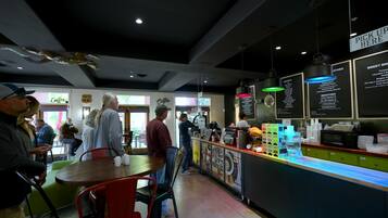 Interior de café com balcão, quadros de menu e área de estar.