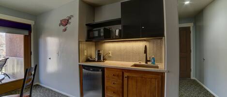 A compact kitchen with a dishwasher, wooden cabinets, and a microwave.