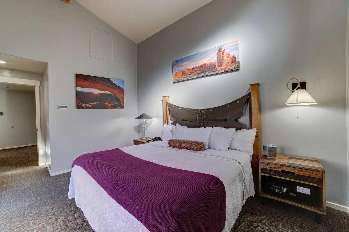 A neatly made bed with a purple blanket, a wooden headboard, and two paintings on the wall.