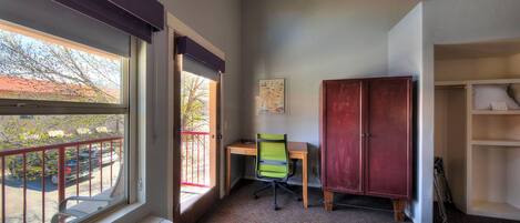 A hotel room with a large window, a desk, a chair, a wardrobe, and a bed.