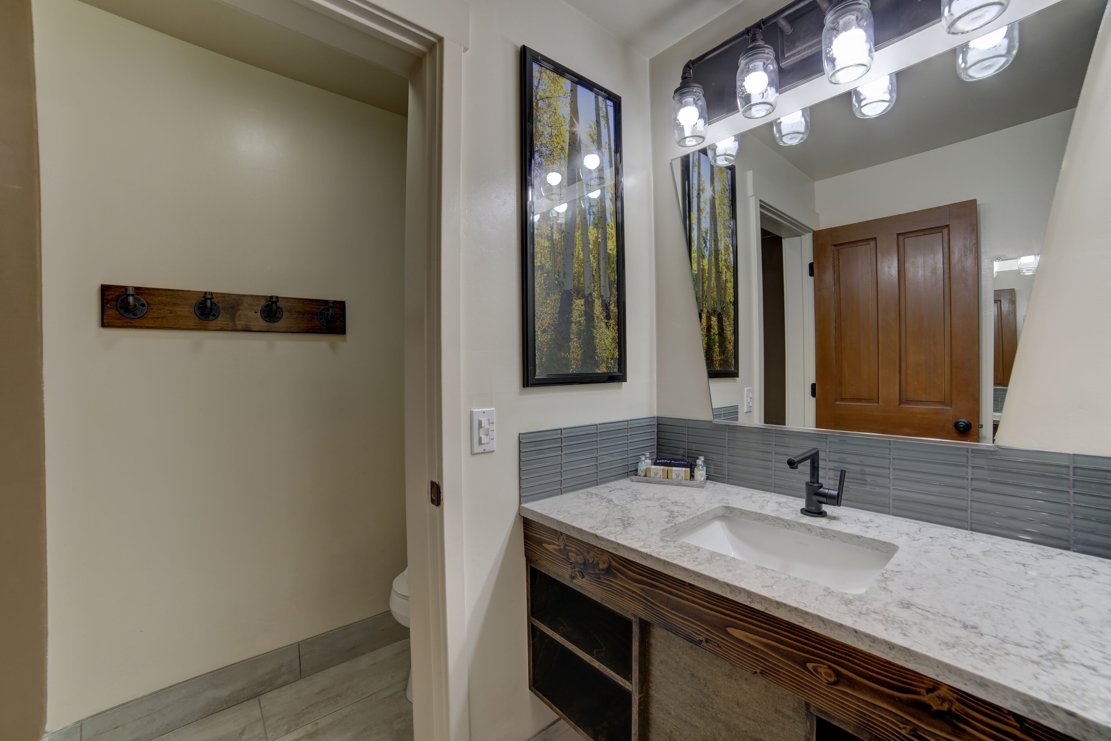 A bathroom with a white sink, wooden vanity, and a large mirror with lights above.