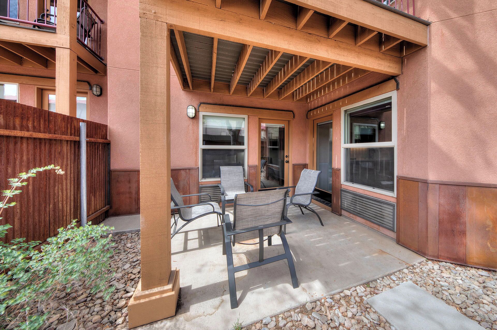 A covered patio with outdoor seating, a wooden fence, and a building with large windows.