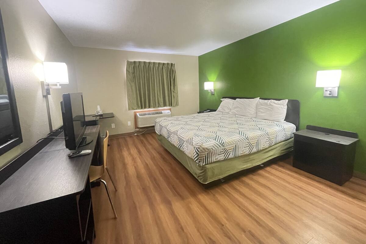 A hotel room with a bed, a desk, a chair, a TV, a lamp, and a nightstand.