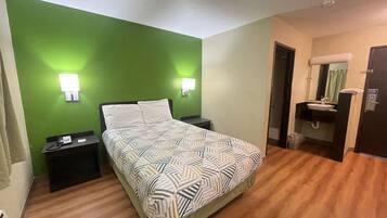 A hotel room with a bed, bedside tables, a green wall, a bathroom with a sink and mirror, and a door.