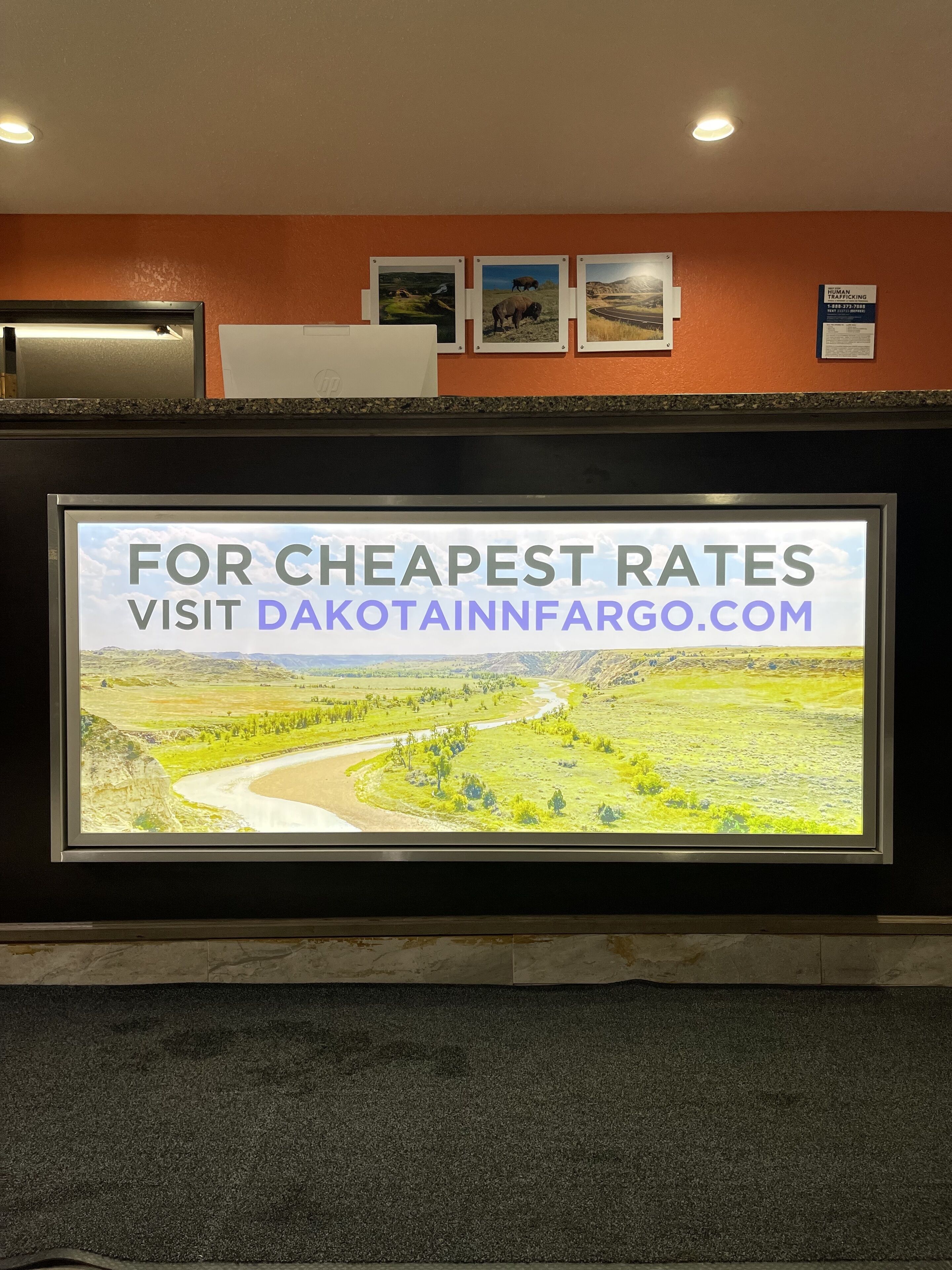 A sign with a landscape view and text advertising the cheapest rates at dakotainnfargo.com.