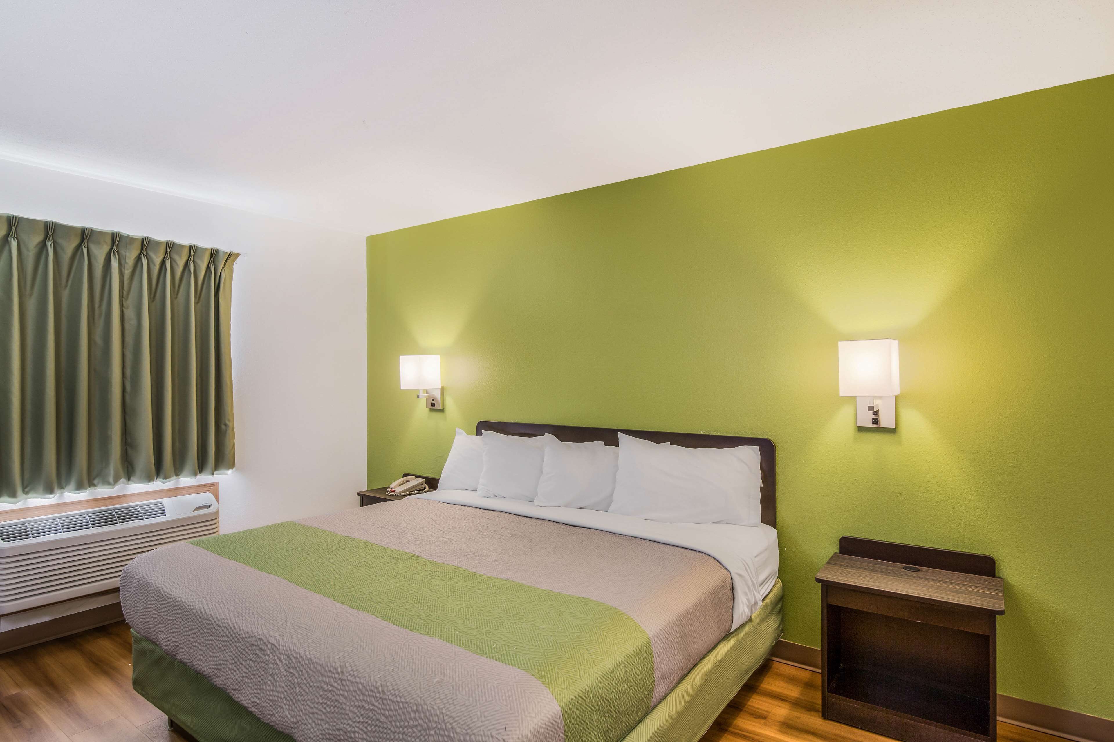 A hotel room with a bed, two bedside lamps, a nightstand, and a window with curtains.