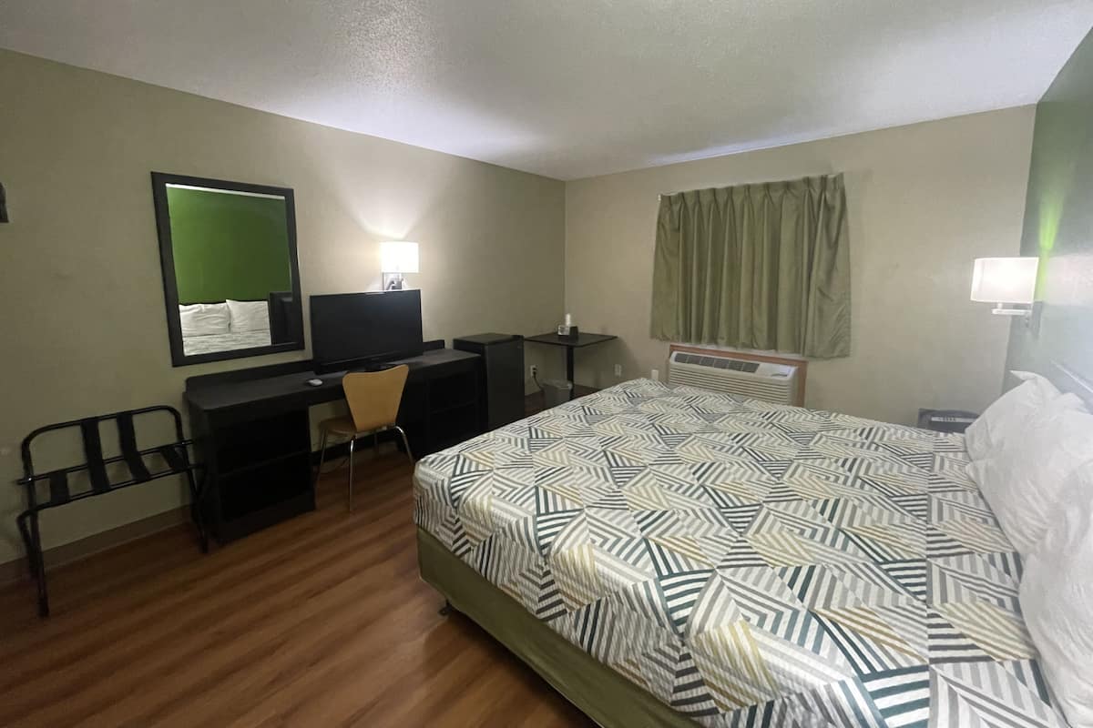 A hotel room with a bed, a desk with a computer, a chair, a television, and a window with curtains.