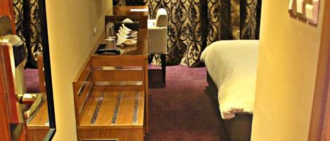 Ein Hotelzimmer mit Bett, Schreibtisch, Stuhl, Spiegel, kleinem Mülleimer und Vorhang.