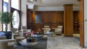 A lobby with multiple seating areas, including sofas and armchairs, arranged around a central coffee table. There are potted plants and a large window providing natural light. - Hotel Belere Rabat (Rabat)