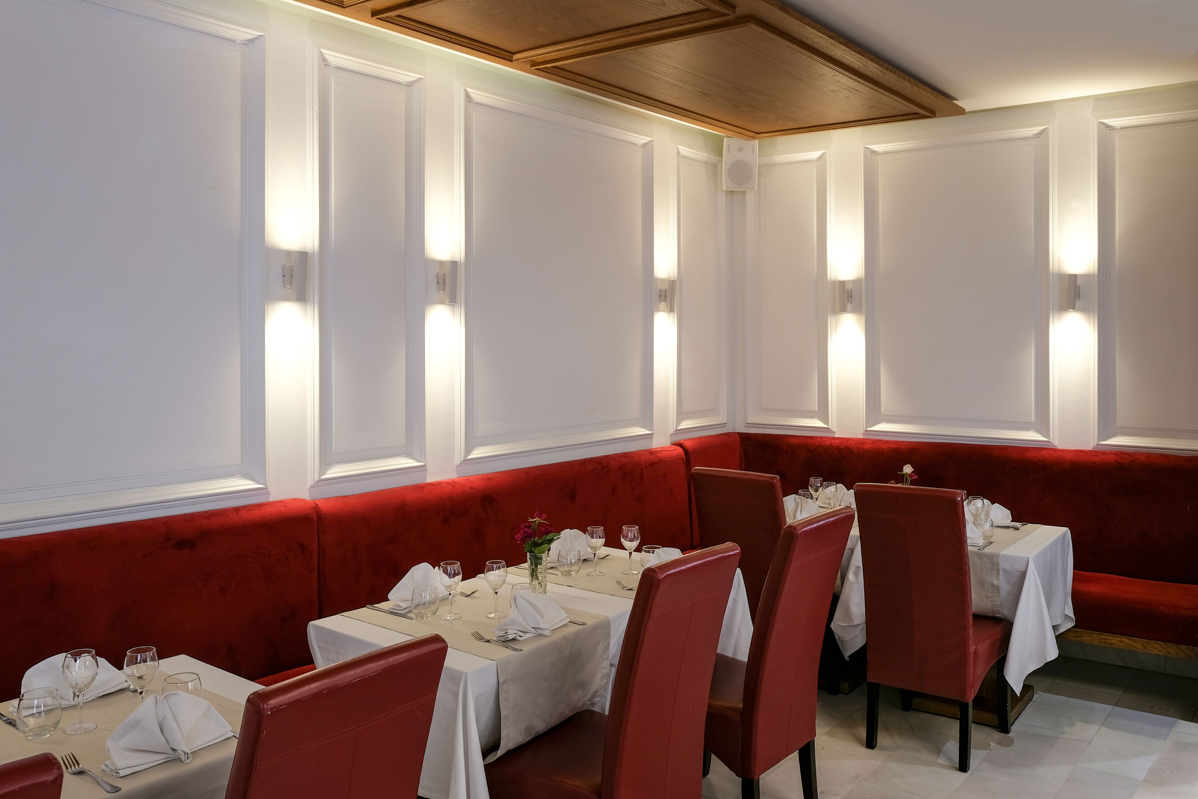 A restaurant with white walls, red upholstered booths, and tables set with white tablecloths and silverware.