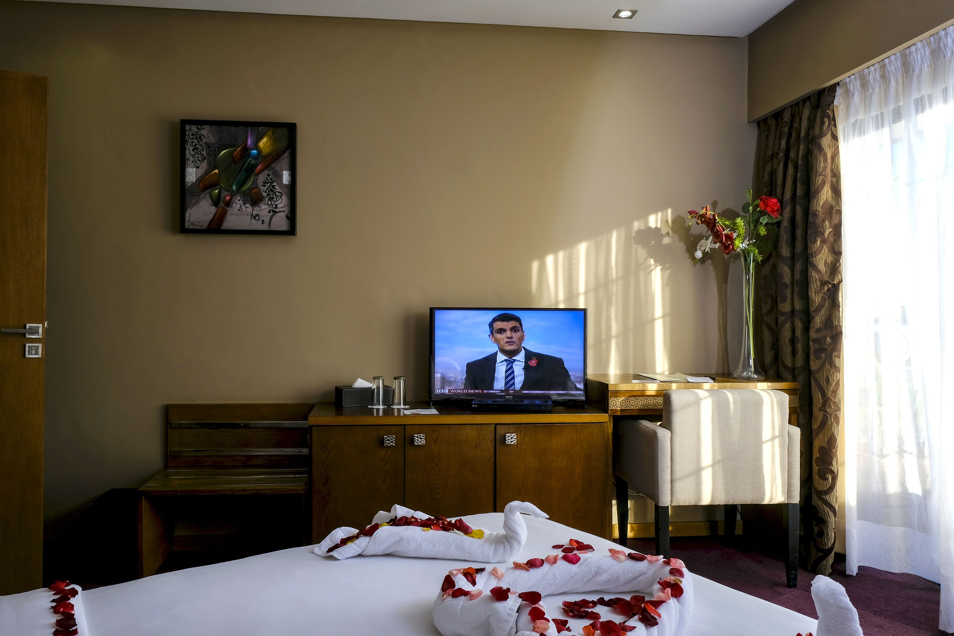 Habitación de hotel con cama, televisión, escritorio y ventana con cortinas.