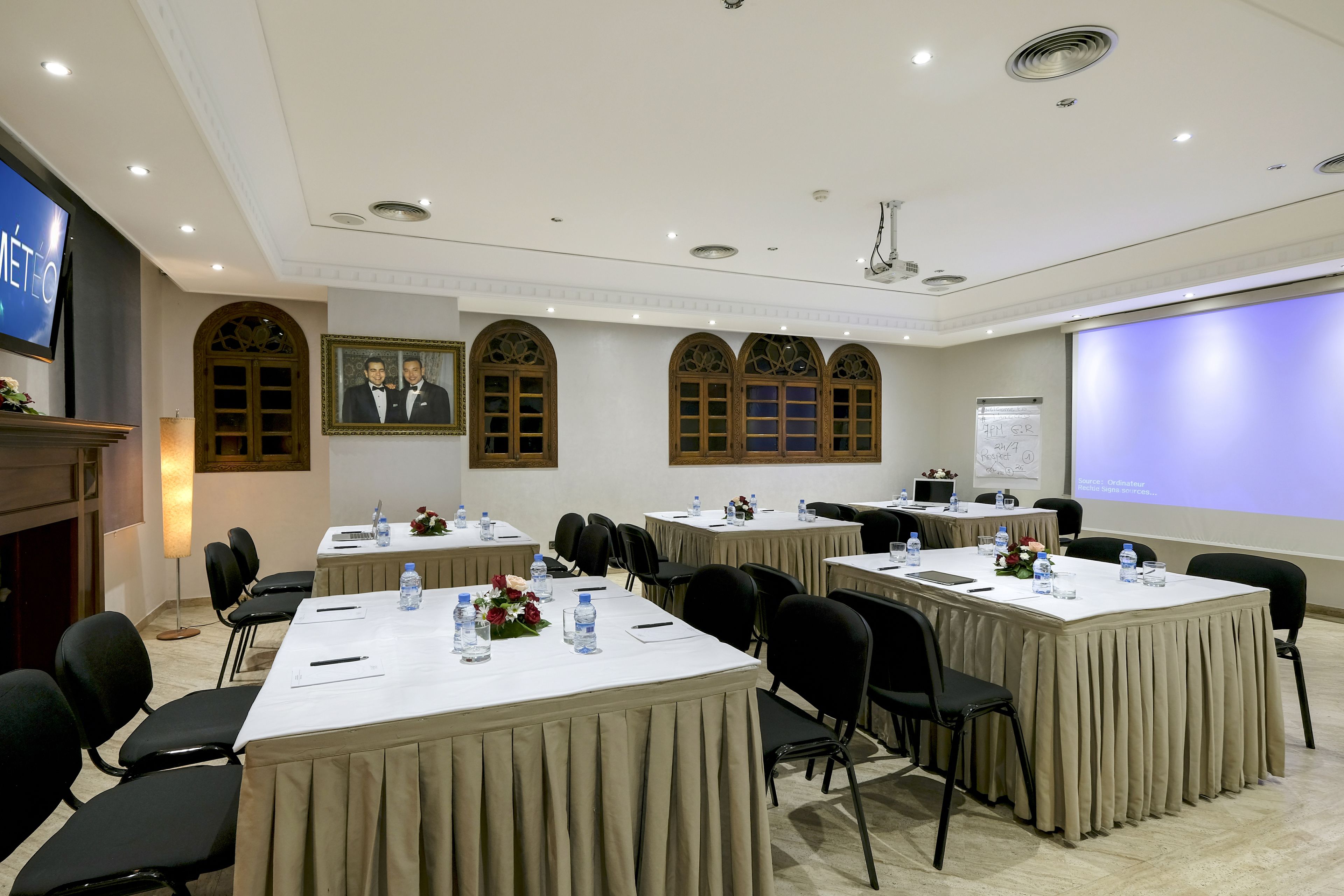 A conference room with multiple tables, chairs, and presentation screens.