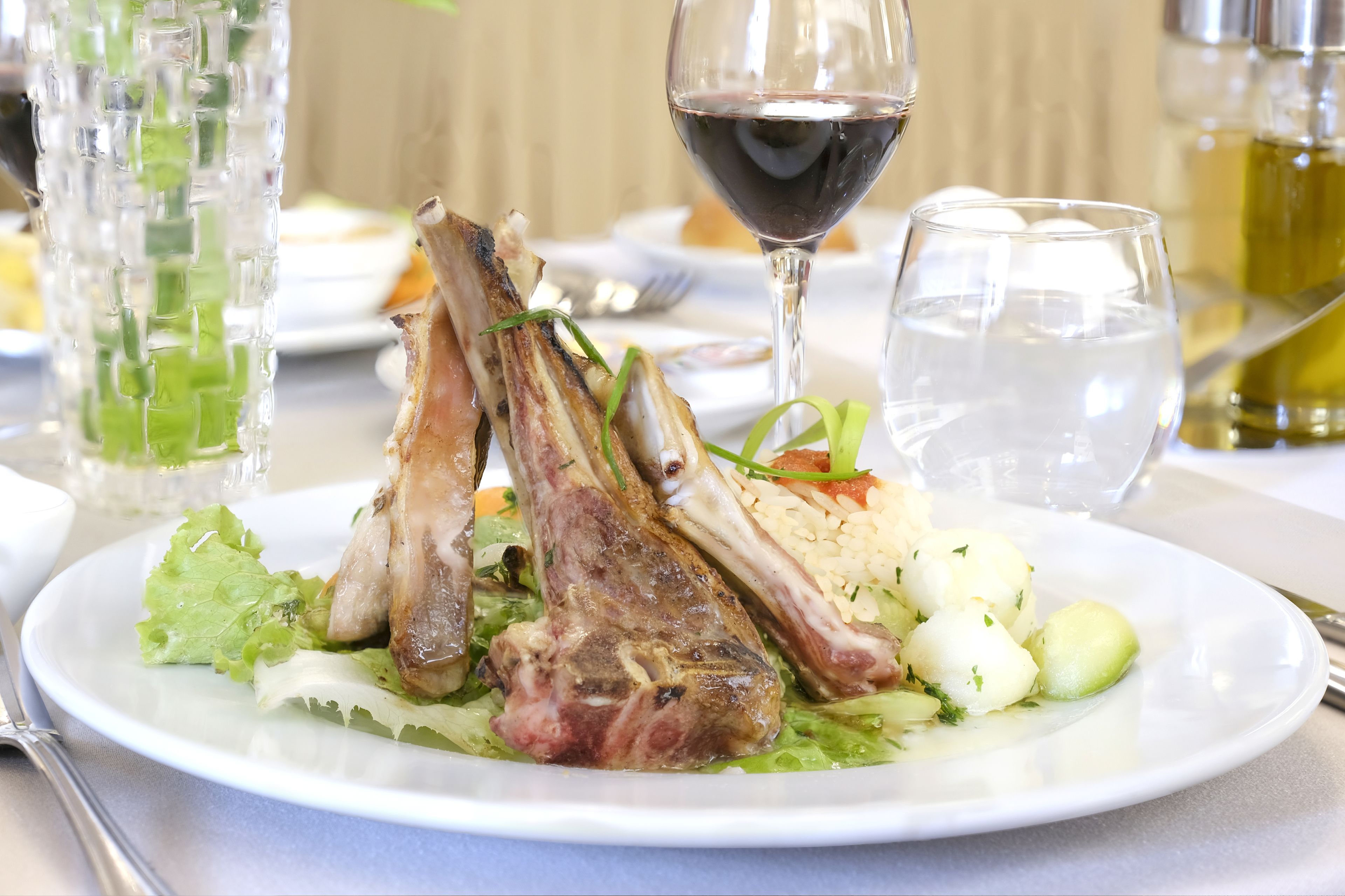 A plate of food with lamb chops, vegetables, and a glass of red wine.