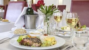 A dining table with a variety of dishes including a steak, rice, and vegetables, along with wine glasses and a bottle of champagne.