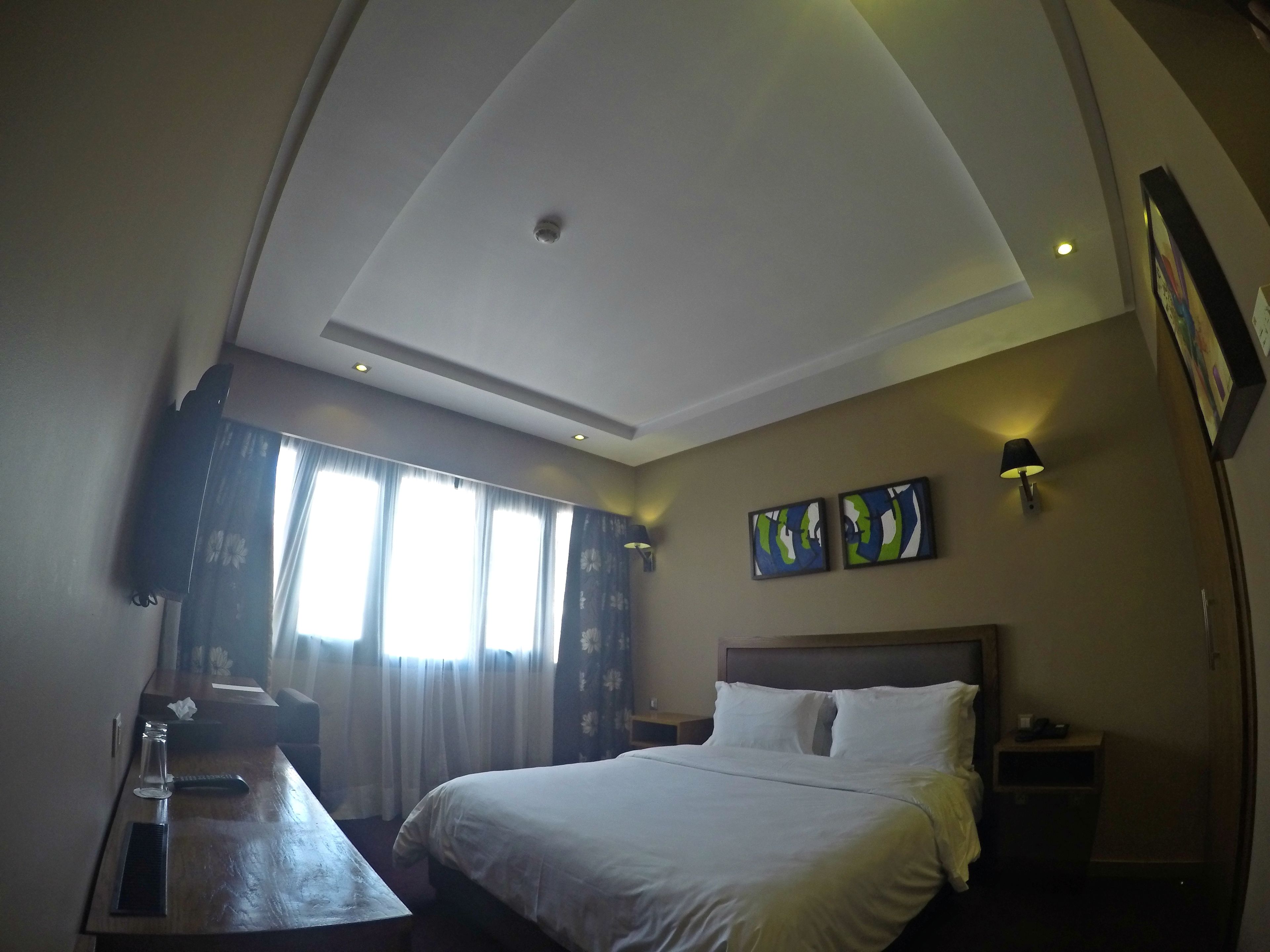 A hotel room with a bed, bedside table, lamp, and artwork on the wall.