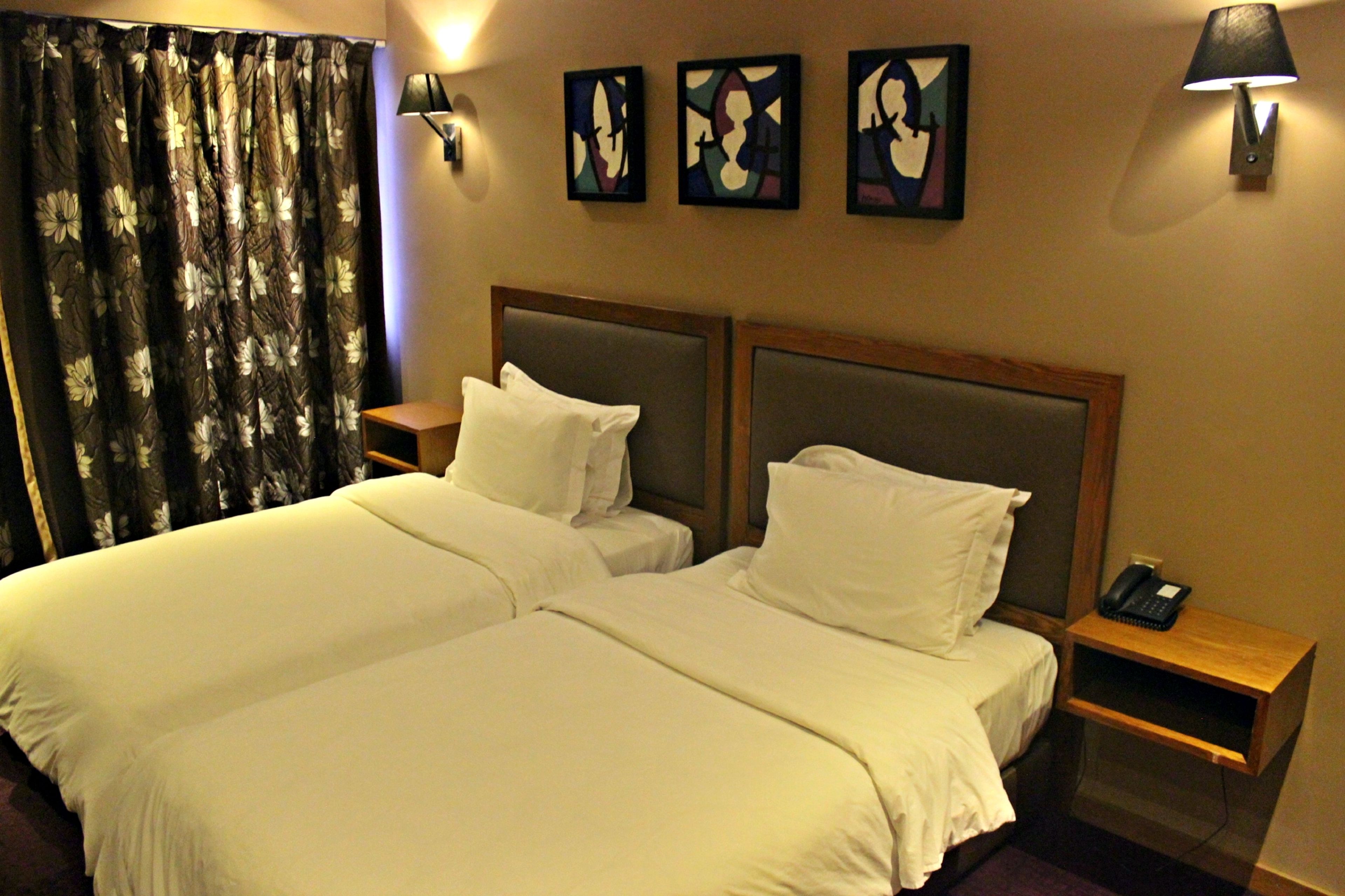 A hotel room with two beds, a nightstand with a phone, and three wall-mounted lamps.