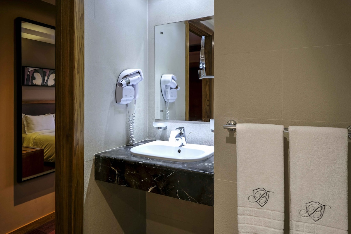 Un baño con un lavamanos, dos secadores de pelo, un espejo y dos toallas con diseños personalizados.