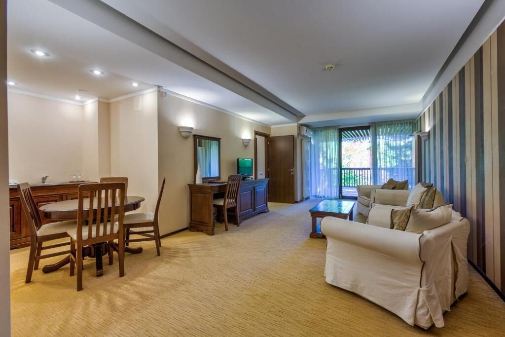 Una sala de estar con un sofá, una mesa de comedor con sillas, un televisor y una ventana con cortinas.