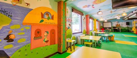 Ein Kinderspielbereich mit bunten Wandgemälden, Tischen und Stühlen.