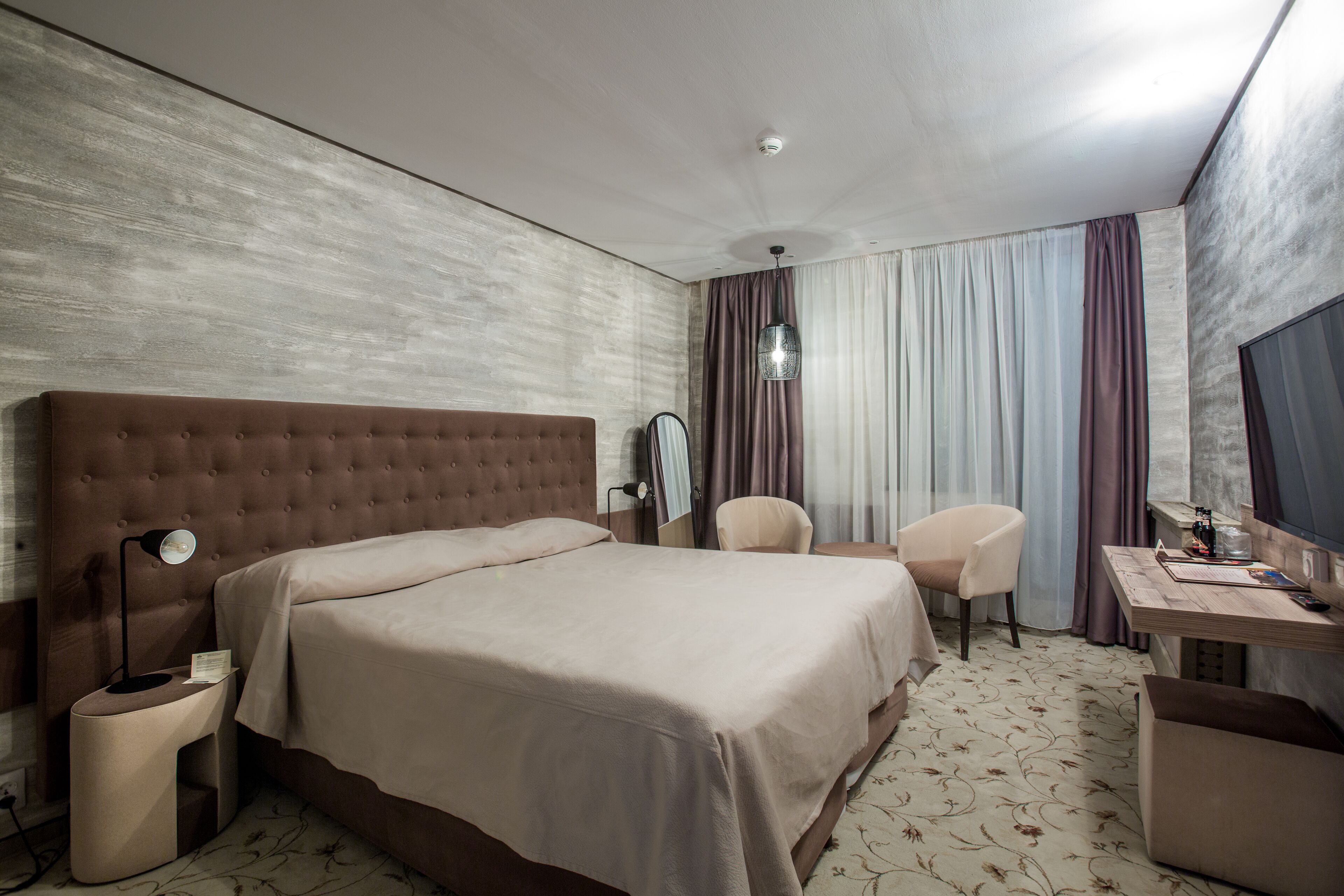 Una habitación de hotel con una cama grande, un escritorio con silla, una mesita de noche y un espejo.