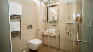 A modern bathroom with a glass-enclosed shower, a toilet, a sink, and a towel rack.