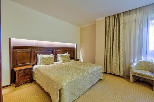 Una habitación de hotel con una cama grande, una mesita de noche, una silla y una ventana con cortinas.