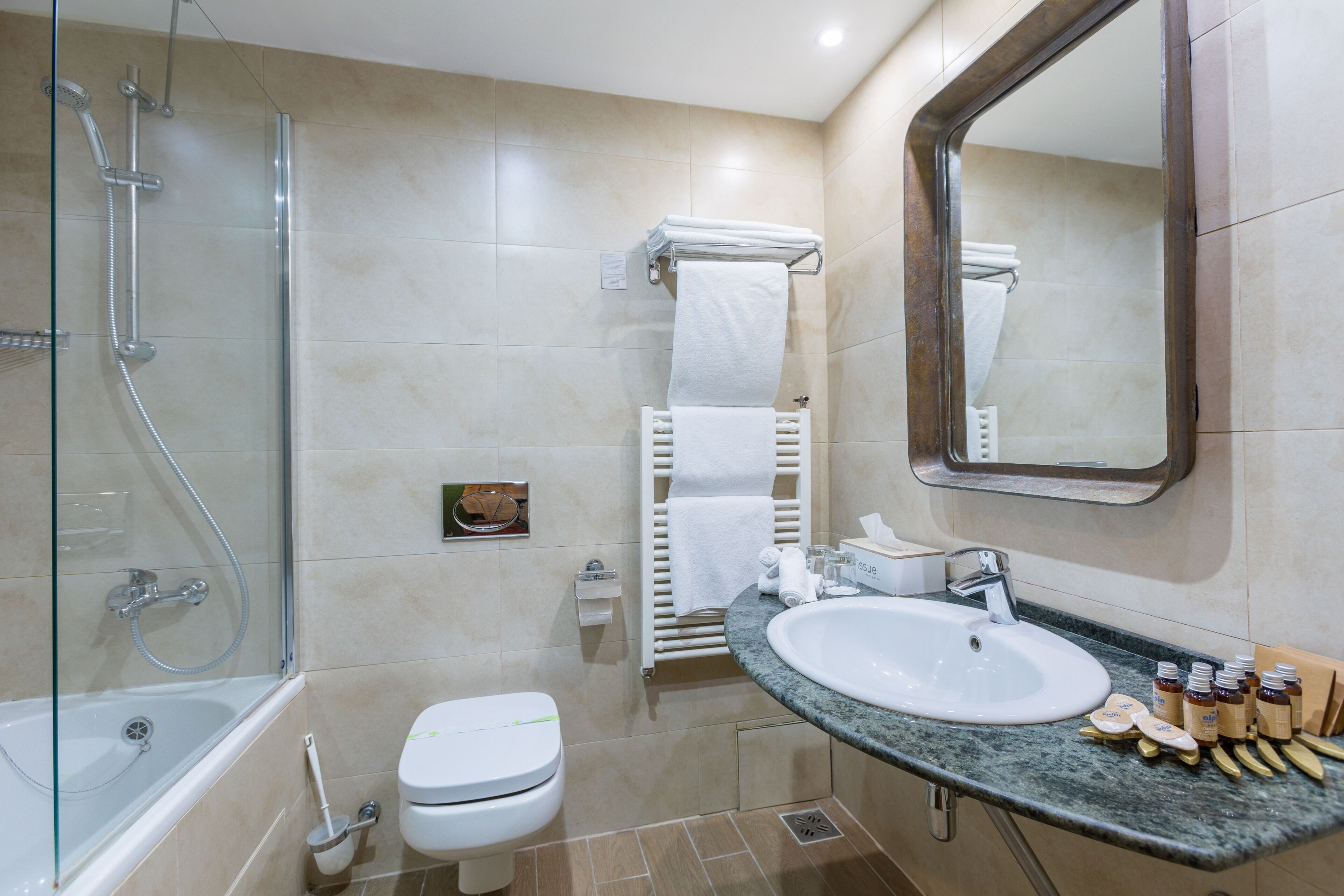 Un baño moderno con ducha envuelta en vidrio, inodoro, lavamanos con artículos de aseo y espejo.