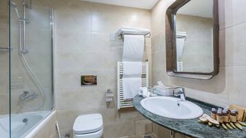 Un baño moderno con ducha envuelta en vidrio, inodoro, lavamanos con artículos de aseo y espejo.