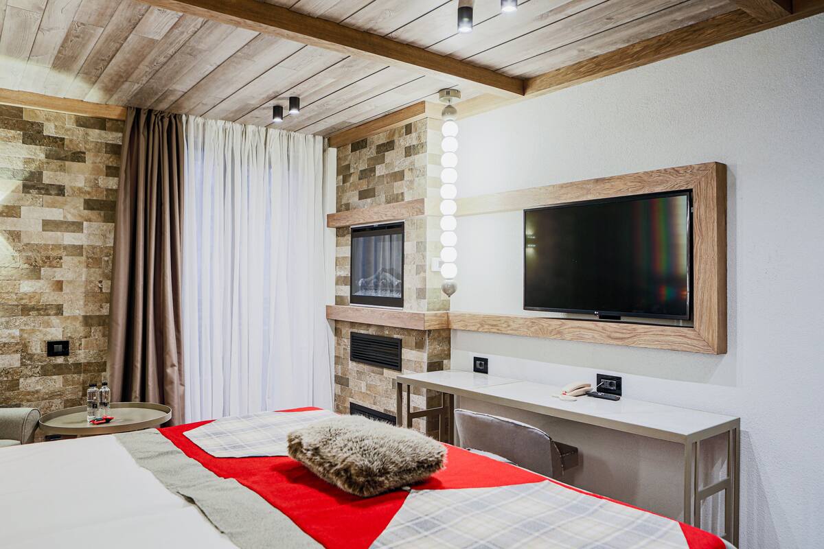 A hotel room with a bed, a desk, a TV, and a stone wall.