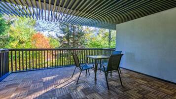 Un espacio al aire libre techado con piso de madera, una mesa con sillas y vistas a árboles y vegetación.