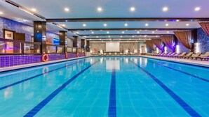 A large indoor swimming pool with clear blue water, surrounded by lounge chairs and a tiled wall with a life buoy. - Alpin Resort Hotel (Brasov)