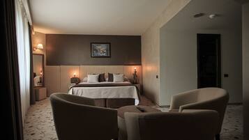 A hotel room with a bed, two chairs, a nightstand, and a painting on the wall.