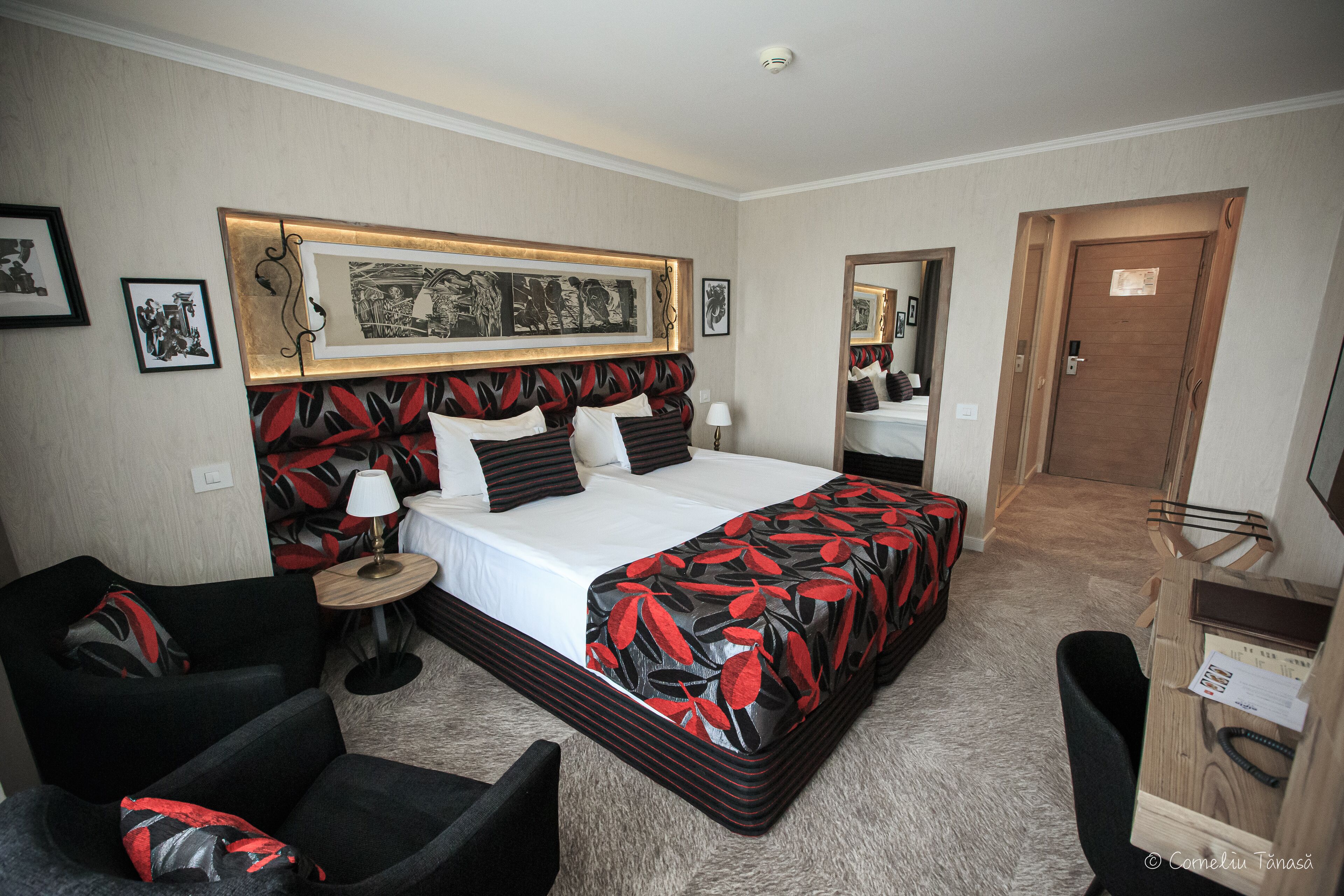 A hotel room with a large bed, a chair, a desk, and a mirror.