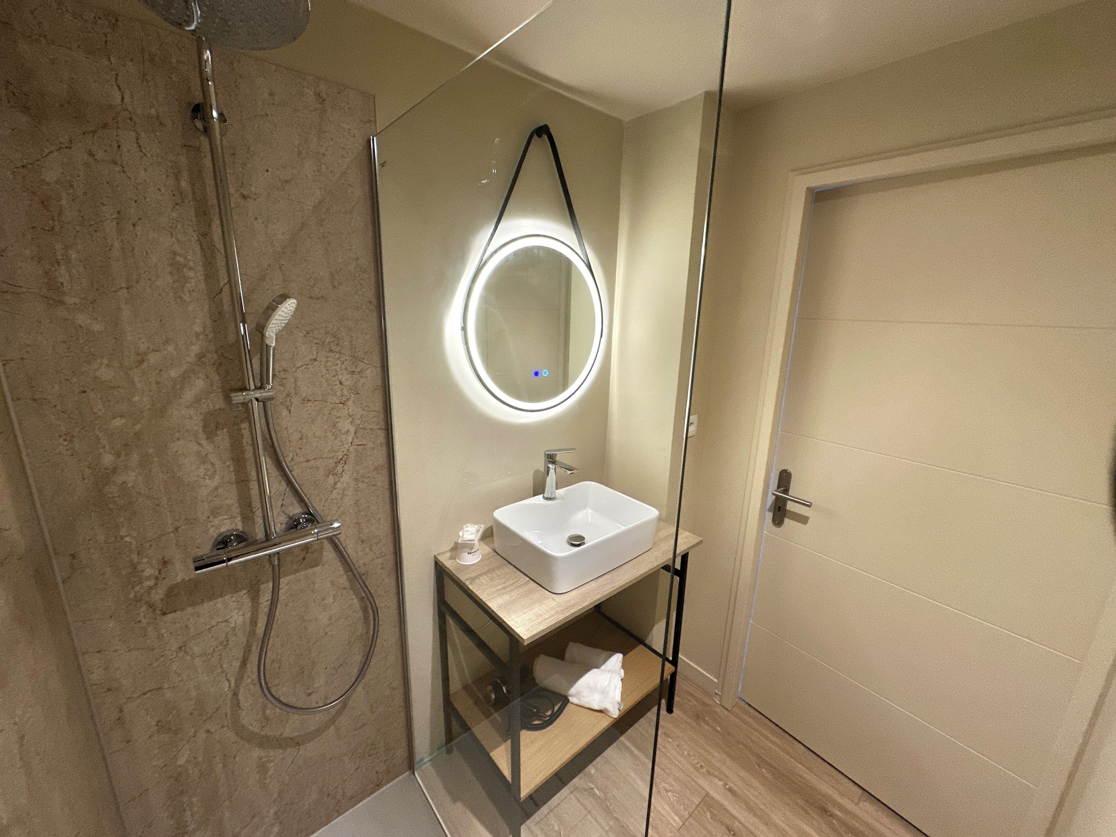 A modern bathroom with a glass-enclosed shower, a round mirror, and a wooden vanity.