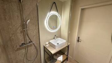 A modern bathroom with a glass-enclosed shower, a round mirror, and a wooden vanity.