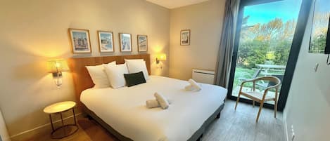 A hotel room with a large bed, bedside lamps, a small table, and a view of the outdoors.