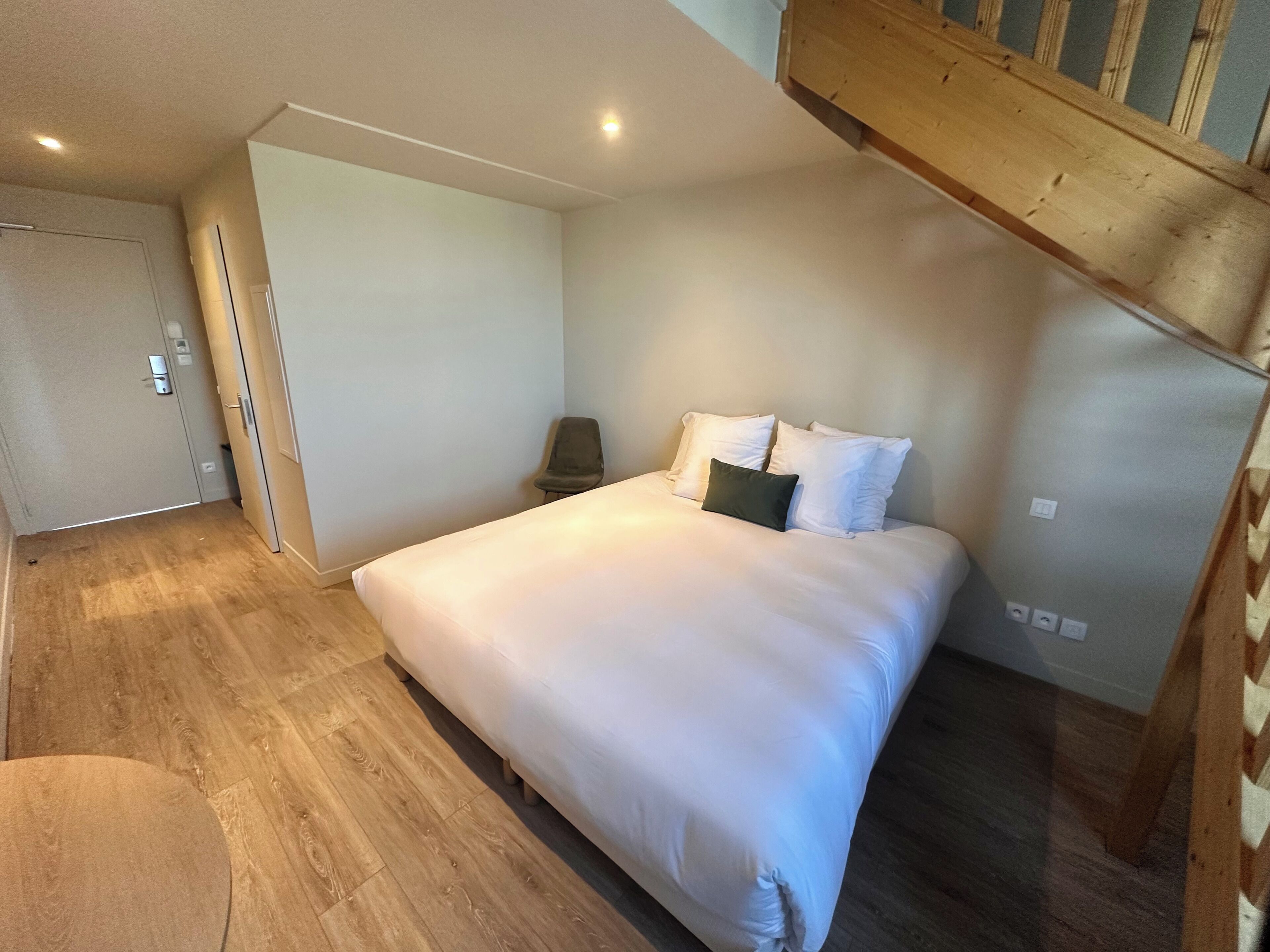 Une chambre à coucher avec un grand lit, une chaise, un banc en bois et une porte.