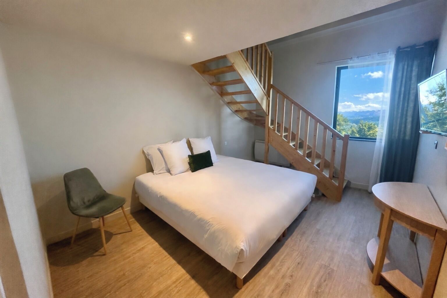 Un dormitorio con cama, una silla, un escritorio, una escalera y una ventana con vistas.