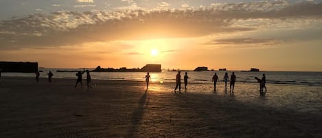 A beach at sunset with people walking and playing.
