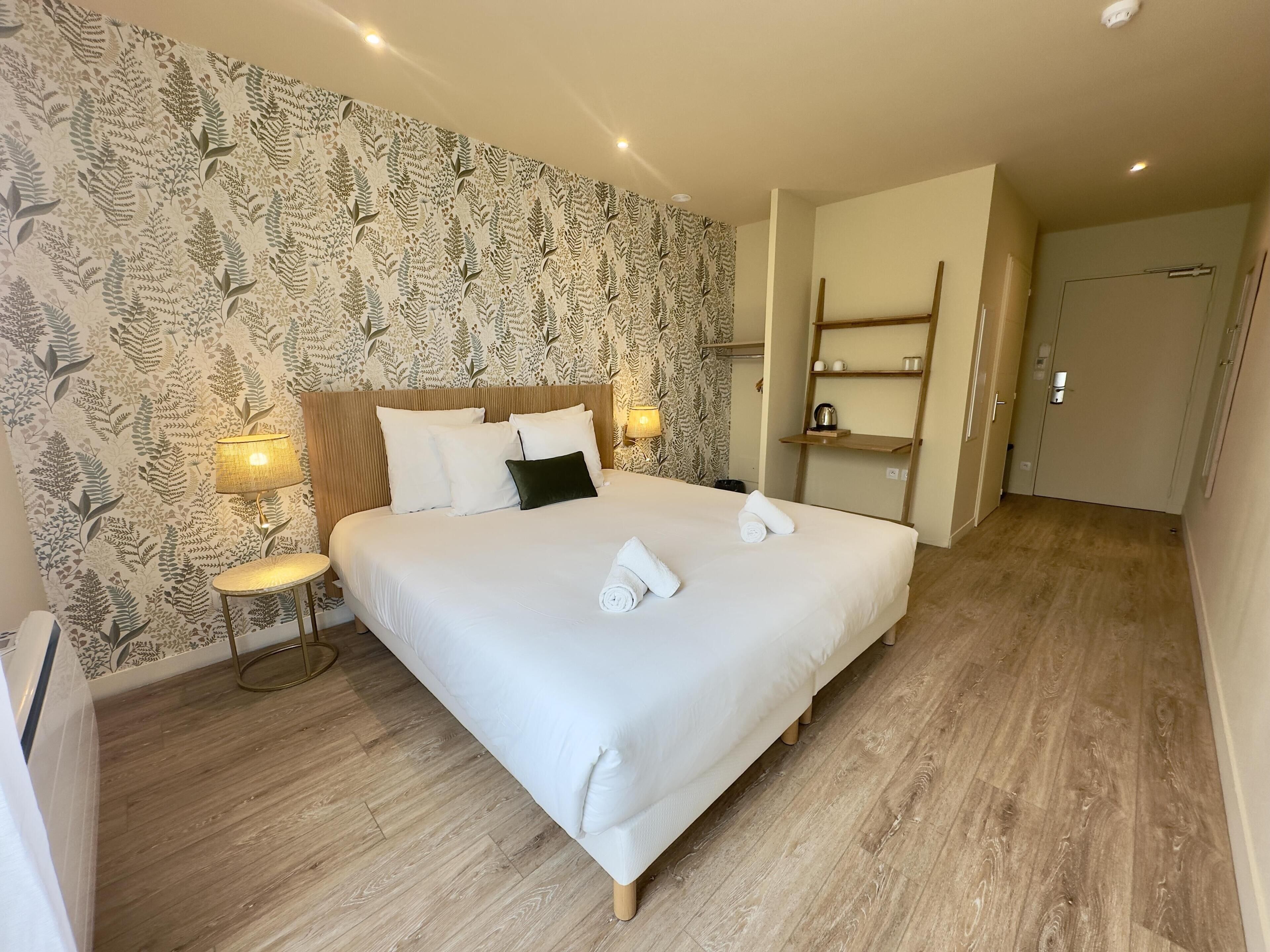 A neatly made bed with white linens and two pillows, a bedside lamp, and a wall with a leafy pattern.