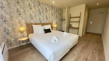 A neatly made bed with white linens and two pillows, a bedside lamp, and a wall with a leafy pattern.