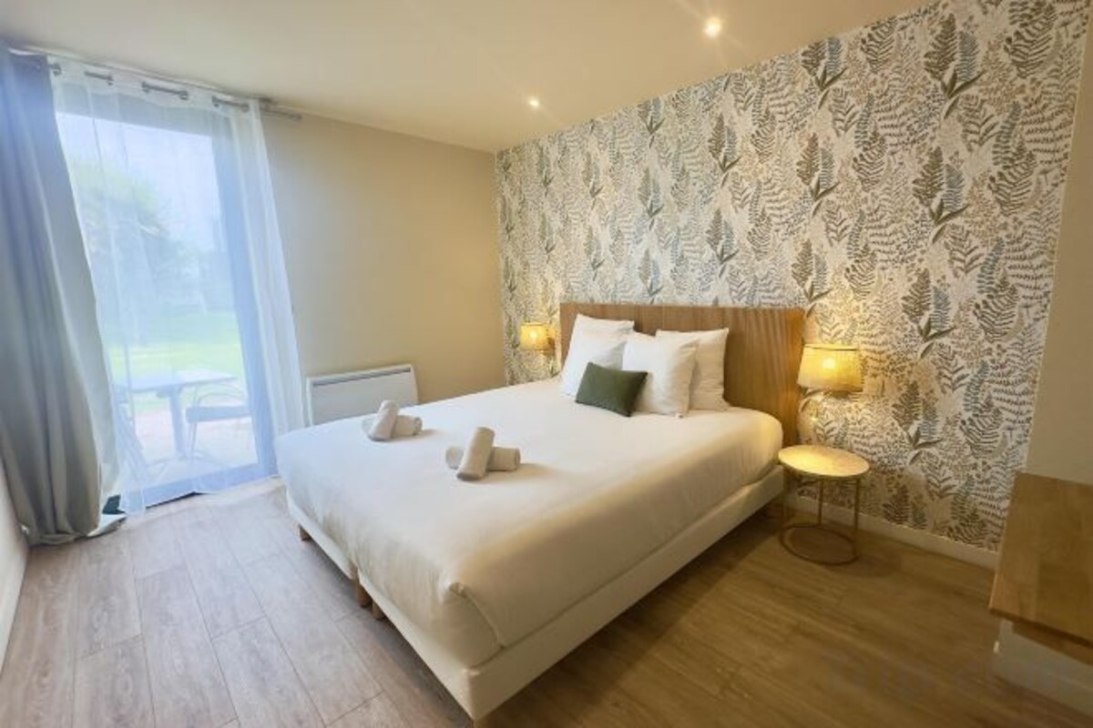 Una camera d'albergo con un letto grande, due lampade ai comodini, carta da parati decorata e vista dalla finestra.