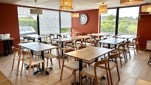 A restaurant with multiple tables and chairs, large windows, and decorative wall panels. - Best Western Hotel de la plage Normandie (Asnelles)