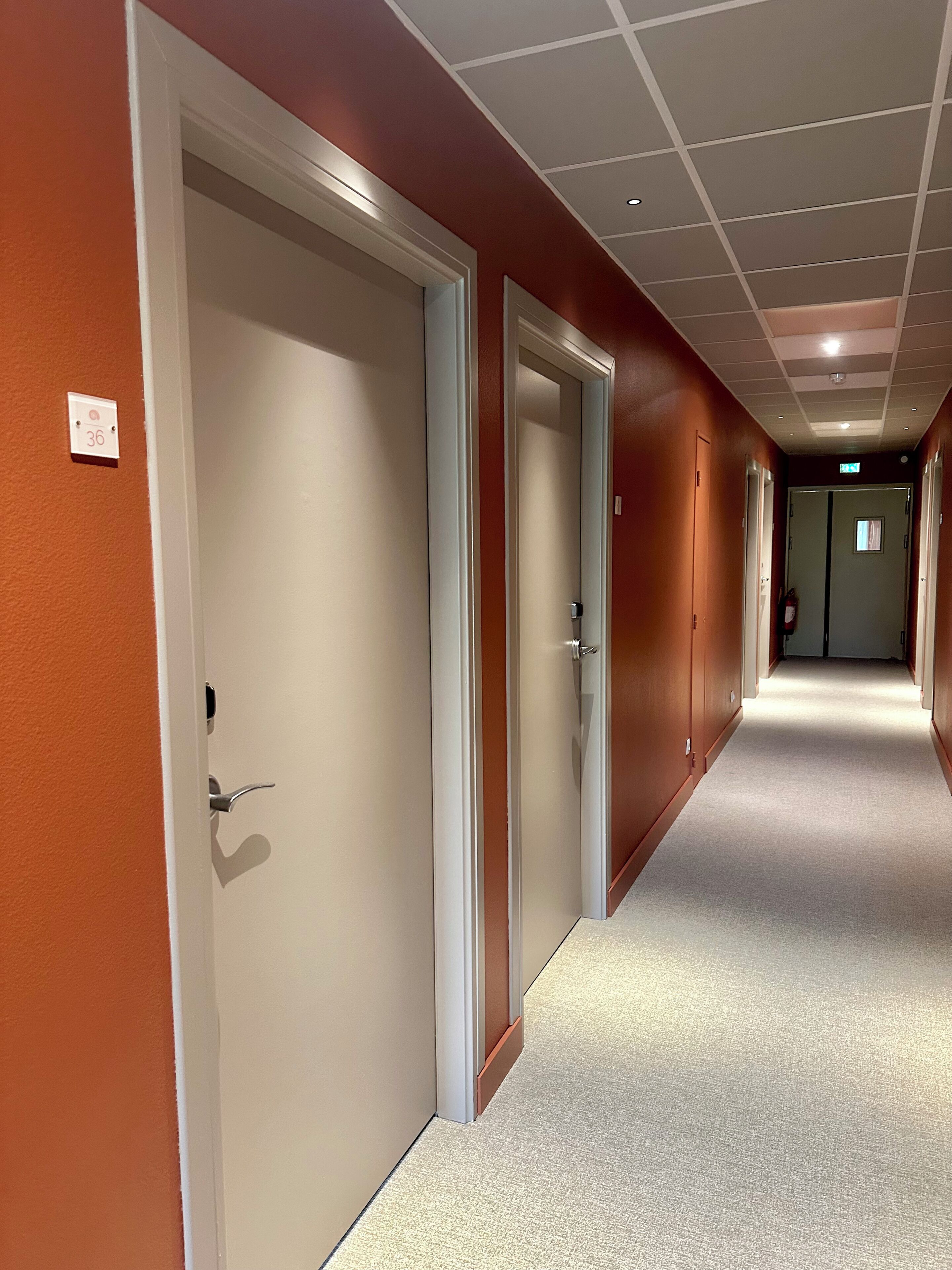 Un pasillo de hotel con puertas cerradas, un extintor y un interruptor de luz en la pared.